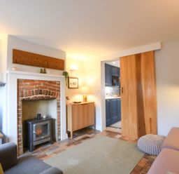 A living room with a fireplace a wood stove TV and a wooden sliding door at Caines Cottage in Westleton