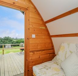 A wooden room with a floral covered sofa and an open door leading to a deck with a picnic table at Badger Set @ Penbugle Organic Farm in St Keyne near Duloe