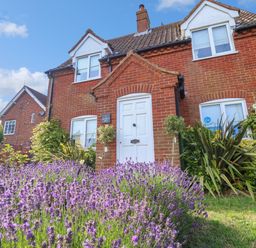 A red brick house with white windows and a white door surrounded by lavender plants at 1 Market Hill in Orford