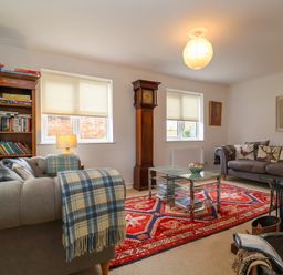 A living room with two sofas a red patterned rug a grandfather clock and a bookshelf at 1 Market Hill in Orford