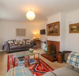 A living room with sofas pillows a glass coffee table a fireplace and paintings at 1 Market Hill in Orford