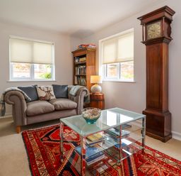 A sitting room with a sofa a glass coffee table a bookshelf a lamp and a tall wooden clock at 1 Market Hill in Orford