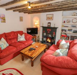 A living room with red sofas a wooden coffee table a fireplace a television and a bookshelf at 4 Lansdown Cottages Bourton-On-The-Water