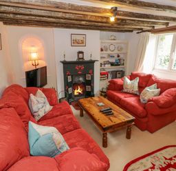 A living room with red sofas wooden coffee table fireplace and bookshelf at 4 Lansdown Cottages Bourton-On-The-Water