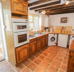 A kitchen with wooden cabinets a double oven a washing machine a small refrigerator and a microwave at 4 Lansdown Cottages Bourton-On-The-Water