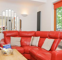 A living room with a red leather sofa a wooden coffee table and a window showing trees at Lodge Nine in Finlake Holiday Park near Chudleigh