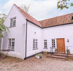 Exterior of a white house with multiple windows a wooden door and a gravel ground with plants at White House Cottage in Little Snoring near Fakenham