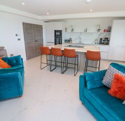 An open-plan kitchen and living area with blue sofas and orange chairs around a kitchen island at 17 Cliff Edge in Newquay