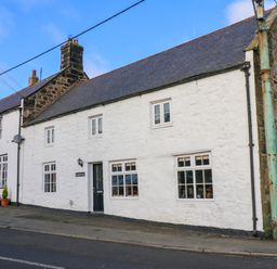 A street view of a white stone cottage with several windows and chimneys at Rose Hip Cottage in Bellingham