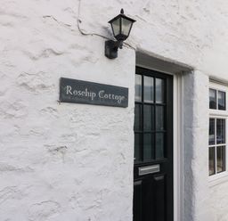 A white textured wall with a black door and window and a sign that says Rosehip Cottage at Rose Hip Cottage in Bellingham