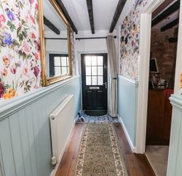 A hallway with floral wallpaper and light blue wainscoting a mirror radiator a rug and a black door at Rose Hip Cottage in Bellingham