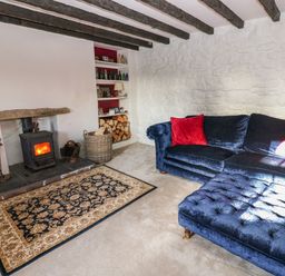 A living room with a wood-burning stove a basket of firewood a blue sofa with red cushions and a patterned rug at Rose Hip Cottage in Bellingham