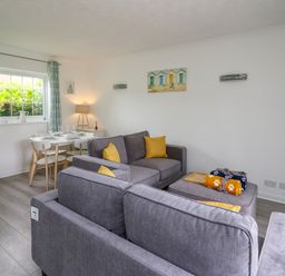 A living room with grey sofas yellow cushions a dining table with chairs and curtains at Sea Rose in Aberporth