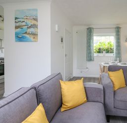 A living area with gray sofas and yellow cushions next to a dining table and kitchen at Sea Rose in Aberporth