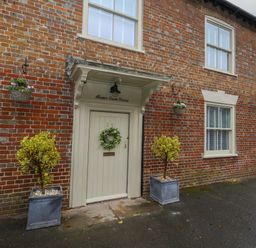 Exterior view of a brick house with a cream door and two windows at Manor Farm House in Bere Regis