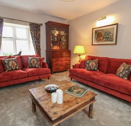 A living room with red sofas a wooden coffee table a wooden cabinet and patterned curtains at Manor Farm House in Bere Regis