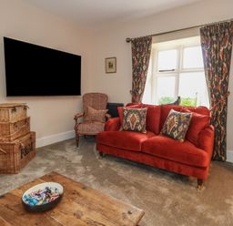 A living room with a red sofa cushions patterned chair a wooden coffee table and a wall mounted television at Manor Farm House Bere Regis