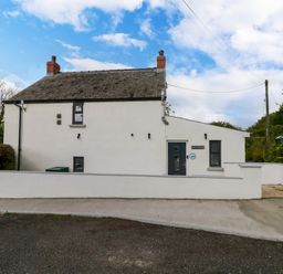 Exterior view of a white cottage with chimney stacks and a stone wall at Folly Cottage in Llanteg near Saundersfoot