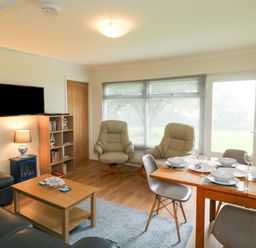 A living room with leather chairs a wooden dining table set with dishes and a wall mounted television at 61 Norton Park in Dartmouth