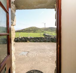 An open door showing a view of a stone wall green fields and hills at Ereiniog 2 in Tremadog