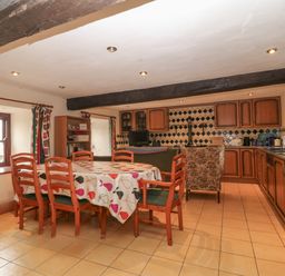 A kitchen with wooden cabinets a tiled floor a dining table with chairs and a stove at Ereiniog 2 in Tremadog
