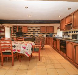 A kitchen and dining area with wooden cabinets a dining table with chairs and tiled floor at Ereiniog 2 in Tremadog