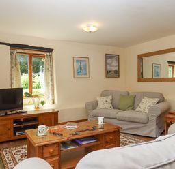A living room with a wooden coffee table and TV stand two sofas a window and a large wall mirror at Peace Cottage Queens Nympton near South Molton