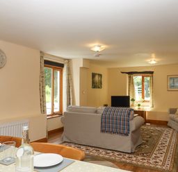 A living room with two beige sofas a TV and a rug near windows and a dining table at Peace Cottage Queens Nympton near South Molton