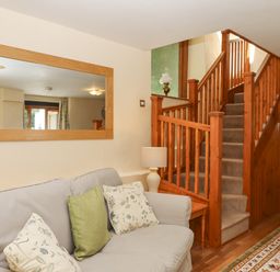 A sitting area with a sofa and cushions next to a carpeted staircase with wooden railing and a wall mirror at Peace Cottage Queens Nympton near South Molton