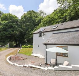 An outdoor patio with chairs and an umbrella next to a white house surrounded by trees at Peace Cottage Queens Nympton near South Molton