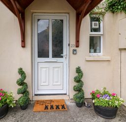 A front door with a doormat and two spiral topiary plants and flower pots on either side at 23 Cois Caol in Skibbereen County Cork