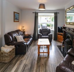 A living room with leather sofas a wooden coffee table a fireplace and a window with curtains at 23 Cois Caol in Skibbereen County Cork