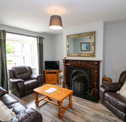 A living room with dark leather sofas a wooden coffee table a fireplace and a TV in the corner at 23 Cois Caol in Skibbereen County Cork