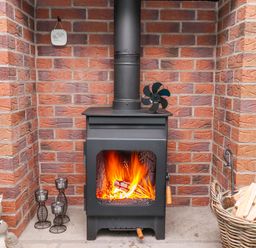 A wood burning stove with fire inside surrounded by brick walls and a basket of firewood at Woodcutters Cottage in Park Village near Haltwhistle