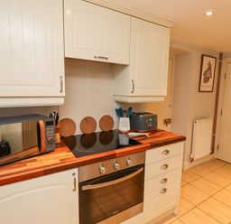 A kitchen with white cabinets a wooden countertop a microwave a stove an oven and a toaster at Woodcutters Cottage in Park Village near Haltwhistle