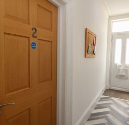 A hallway with a wooden door numbered 2 a notice board on the wall and a white front door at Flat 2 - Studland in Bournemouth