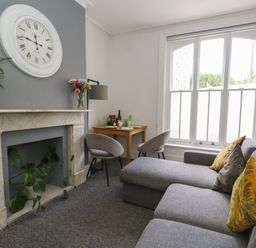 A sitting room with a gray sofa yellow cushions and a marble fireplace with a large wall clock at Flat 2 - Studland in Bournemouth