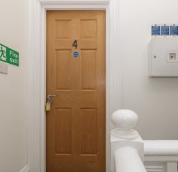 A wooden door numbered 4 in a hallway with fire exit sign and a white safety box at Flat 4 - Hengistdury in Bournemouth
