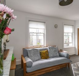 A sitting area with a grey sofa and cushions next to two windows with blinds at Flat 4 - Hengistdury in Bournemouth