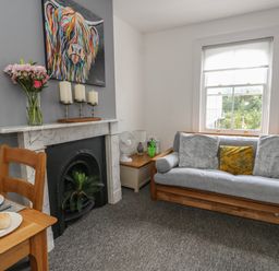 A living room with a wooden sofa with cushions a marble fireplace and a wooden dining table at Flat 4 - Hengistdury in Bournemouth