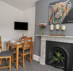 A dining area with a wooden table and chairs a marble fireplace with candles and plants and a wall mounted television at Flat 4 - Hengistdury in Bournemouth