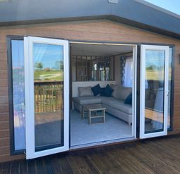 An open patio door revealing a corner sofa with cushions a wooden coffee table and a carpeted floor at Hazel Lodge in Whitby
