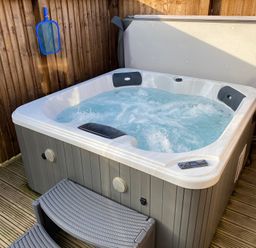 A bubbling hot tub with step stool in a wooden enclosed outdoor area at Juniper Lodge in Whitby