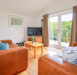 A living room with two brown leather sofas a wooden coffee table a television and glass doors leading to a balcony at 3 Lake View in Lanreath