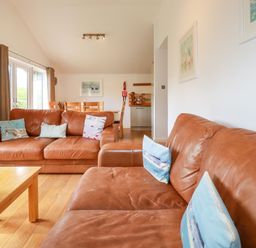 A living room with two brown leather sofas a wooden coffee table and dining table at 3 Lake View in Lanreath