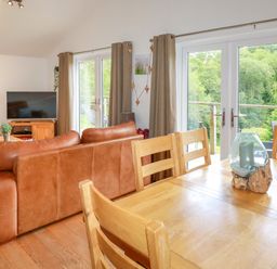 A living room with brown leather sofas wooden dining table and chairs and a television at 3 Lake View in Lanreath