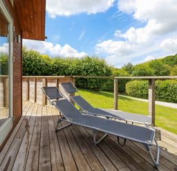 A wooden deck with two lounge chairs overlooking a grassy area and trees at 1 Hedgerows in Lanreath