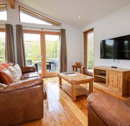 A living room with brown leather sofas wooden furniture and a wall mounted television at 1 Hedgerows in Lanreath