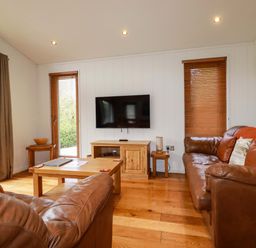 A living room with leather sofas a wooden coffee table a wall-mounted television and wooden blinds at 1 Hedgerows in Lanreath