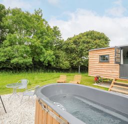 An outdoor area with a hot tub a small table with two chairs two wooden lounge chairs and a wooden cabin at Bracken Broad Langdon near Wainhouse Corner